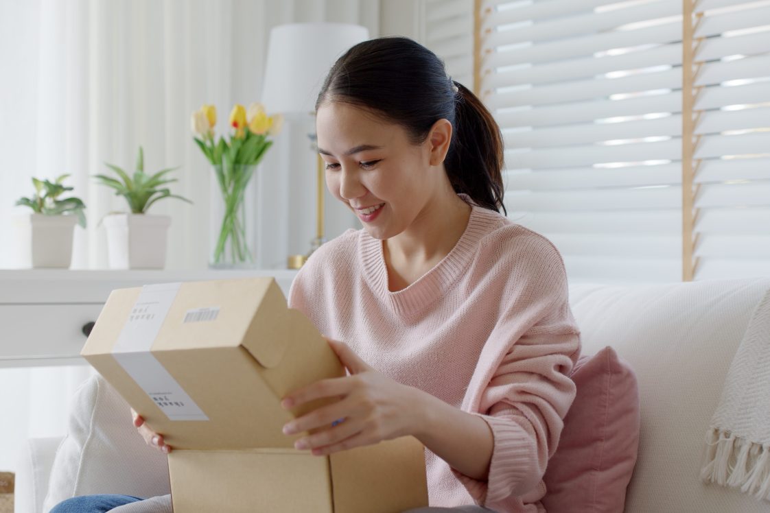 smiling young woman opening up a package in her living room