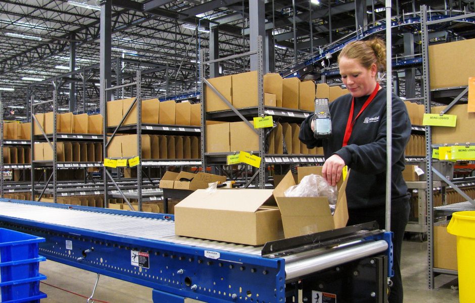 fulfillment center worker scanning a package on a moving line