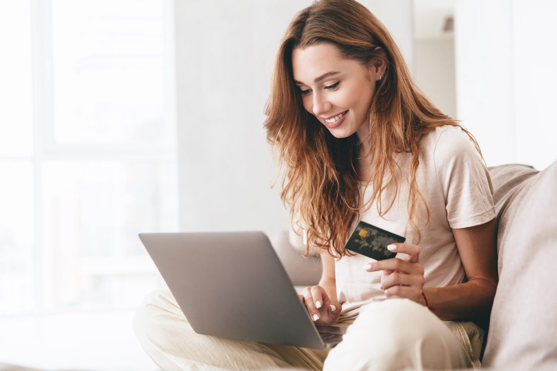 smiling woman shopping on laptop with here credit card out