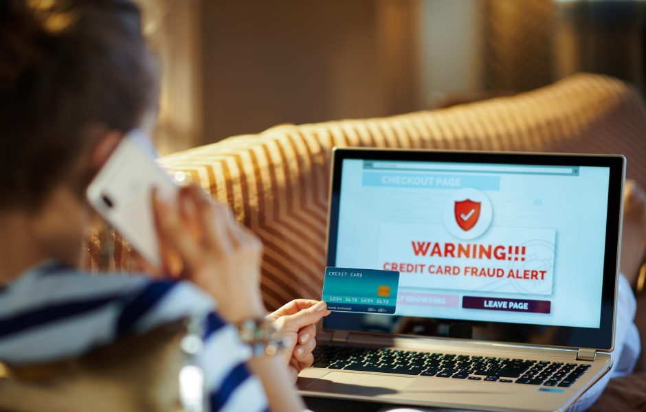 woman shopping on laptop on the phone with a fraud alert warning on her computer screen