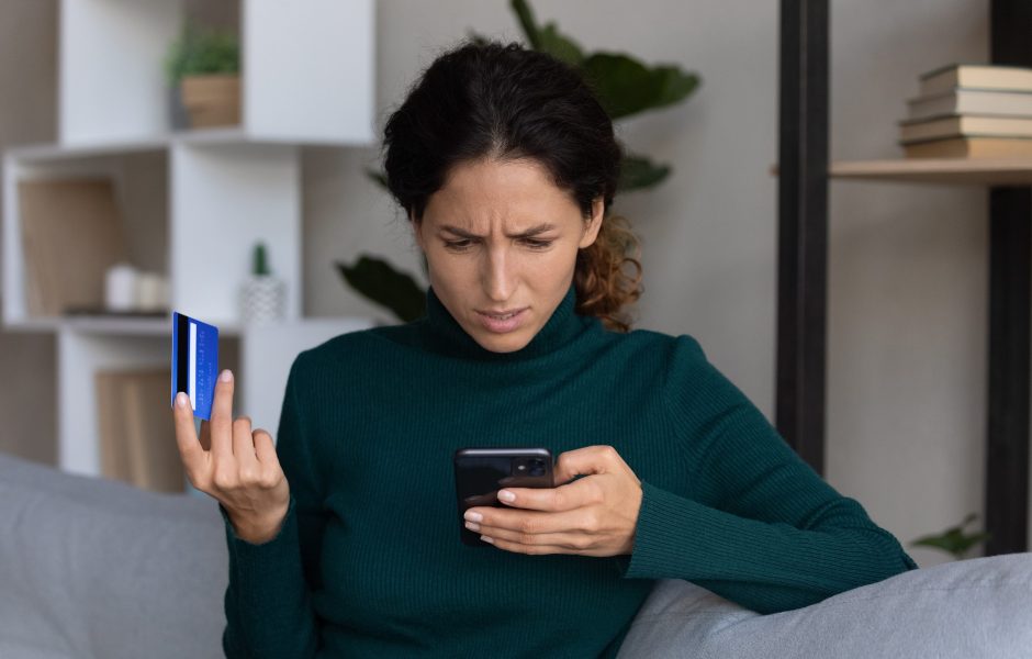 woman with perplexed look on her face looking at phone with credit card in hand