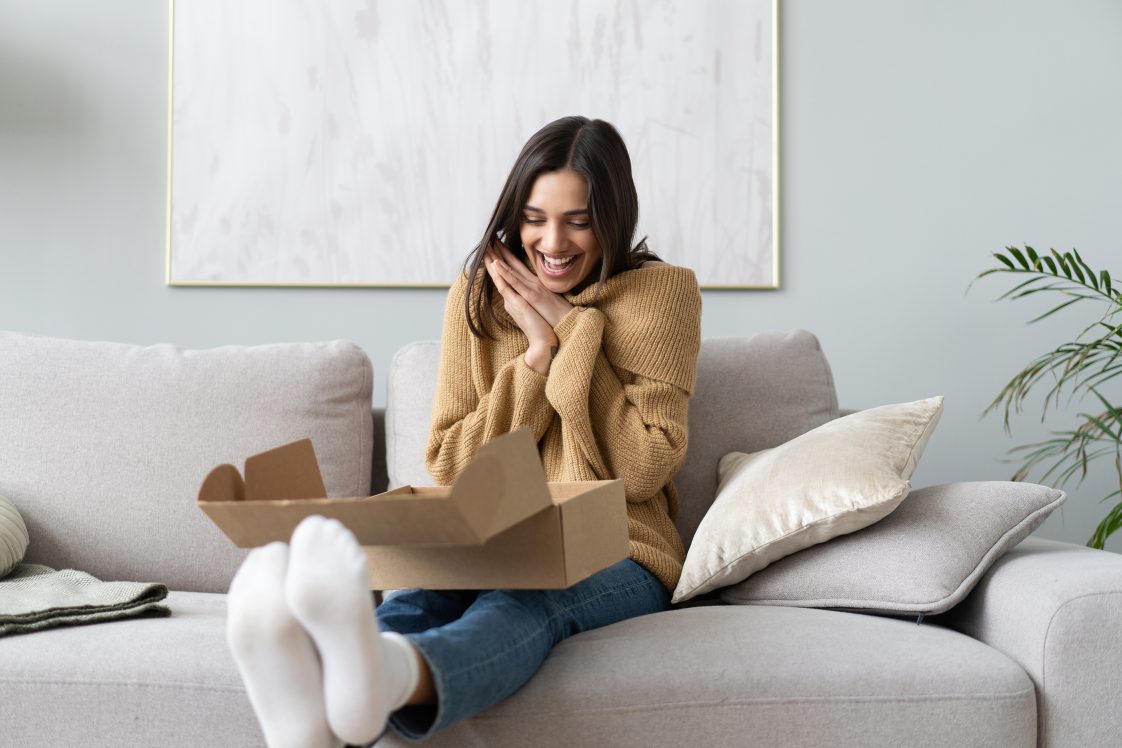 gleeful woman opening up package on couch