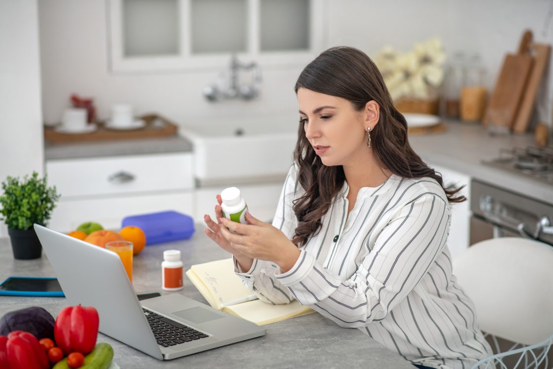 woman on laptop reading back of supplement bottle