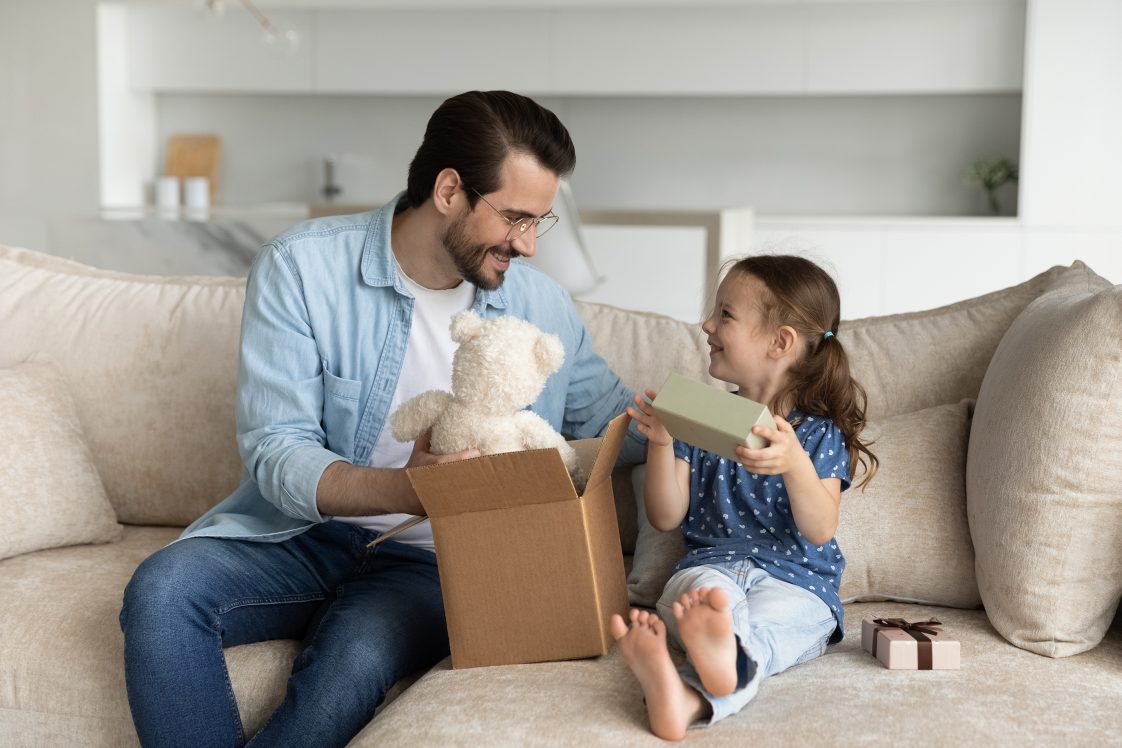 man and daughter opening up a brown box package with a teddy bear inside
