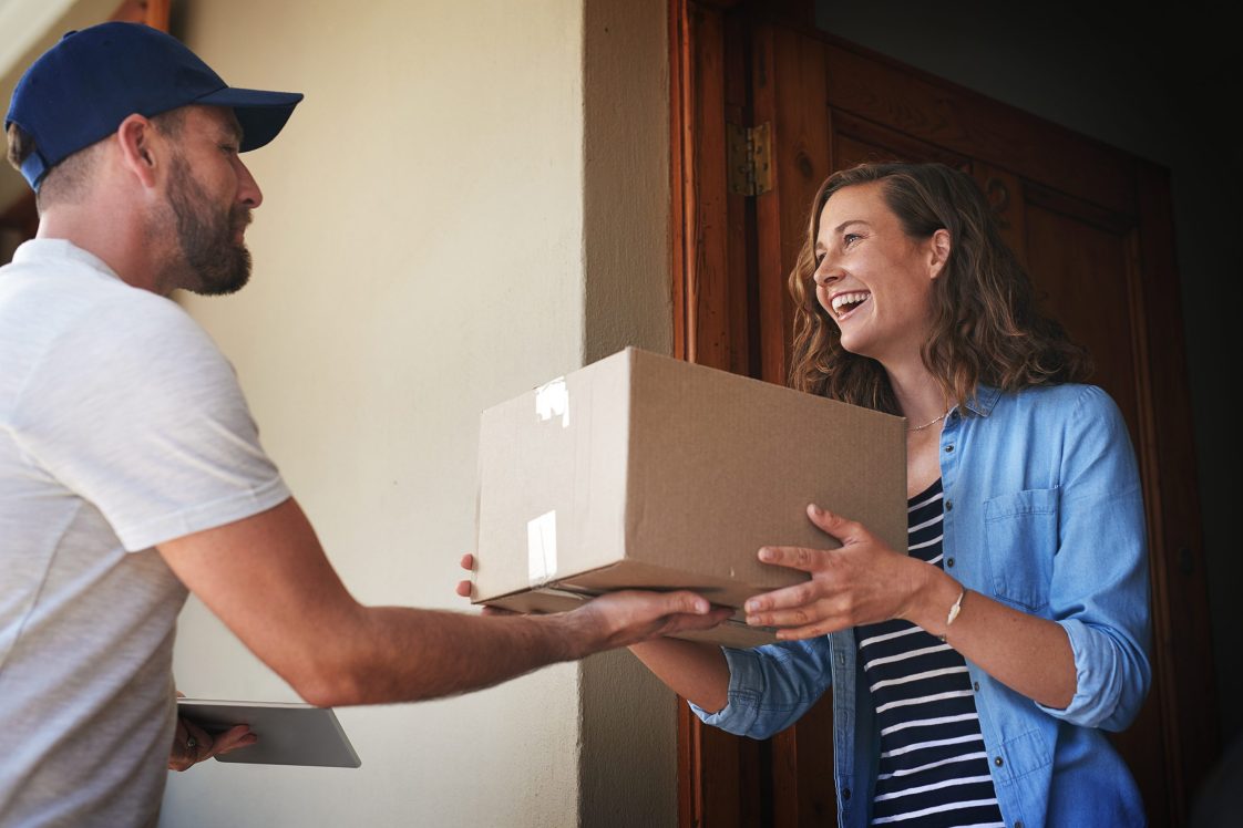 smiling woman at front door getting package from delivery driver