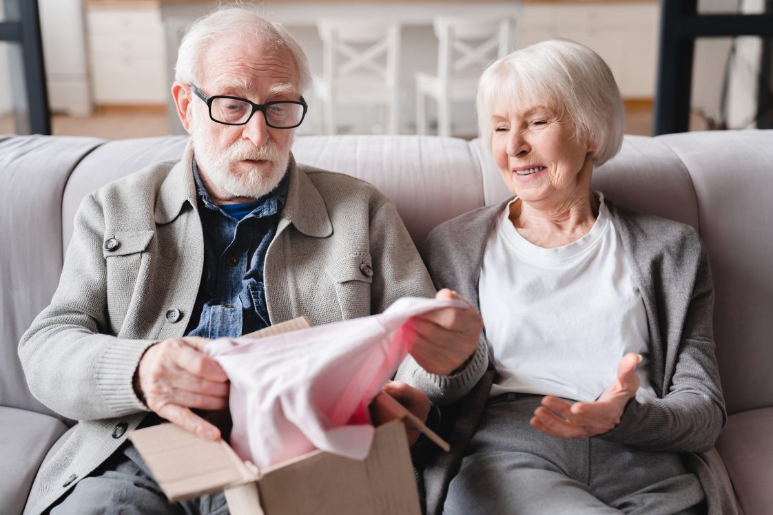 elderly couple opening a package on a couch