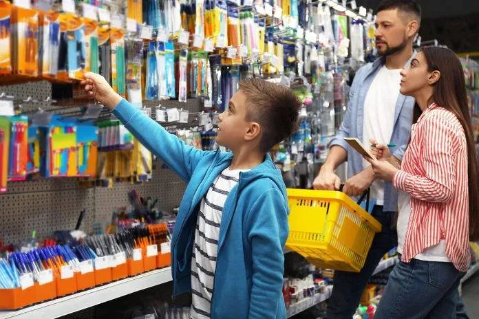 Family with little boy choosing school stationery in supermarket
