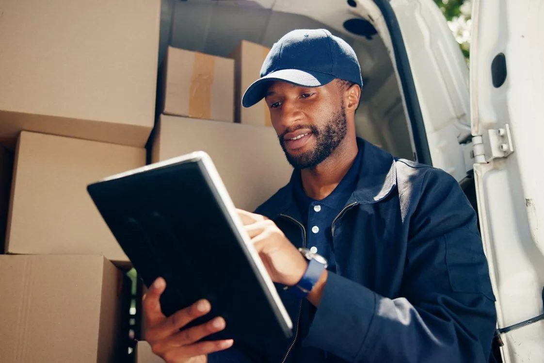 Courier, cargo or man with tablet by van for package distribution, online order checklist or supply chain. Logistics, transport or black driver with digital app for parcel location or inventory check